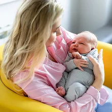 A mother in pink holding her newborn in a yellow armchair