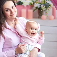 A mother holding her baby beside pink flowers